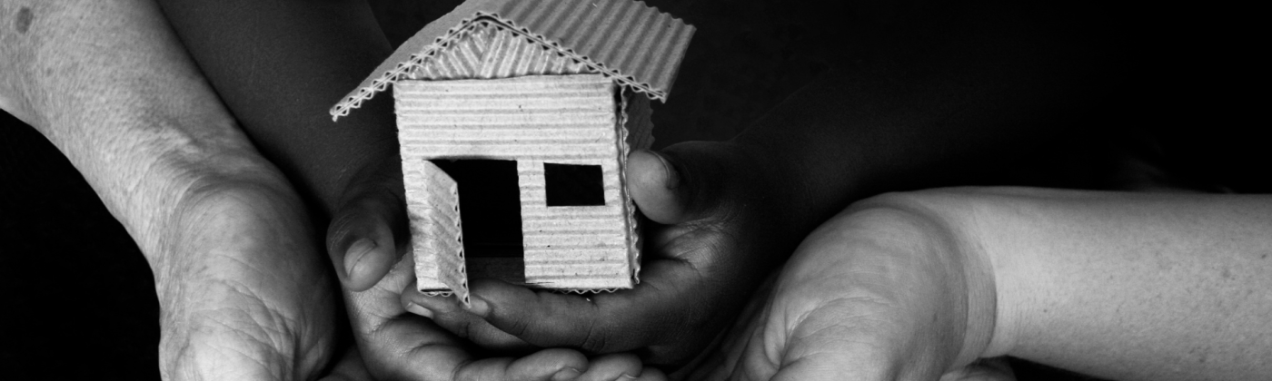 Image of three people's hands laid on top of each other, cradling a small wooden house