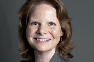 A smiling woman in a gray suit against a gray background