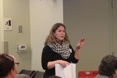 A woman in a graphic scarf, standing in front of people making a presentation.
