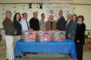 A line of people stand behind a table with three large plastic bins full of candy.