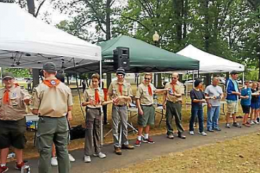 A line of boy scouts in front of tents.