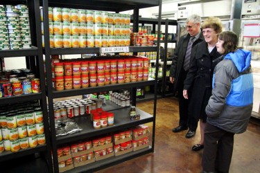 Three people looking at fully stocked food pantry shelves.