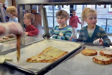 Kids in a cafeteria line getting pizza.