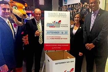 Four people and a person in a mascot costume, standing by a box for food donations.